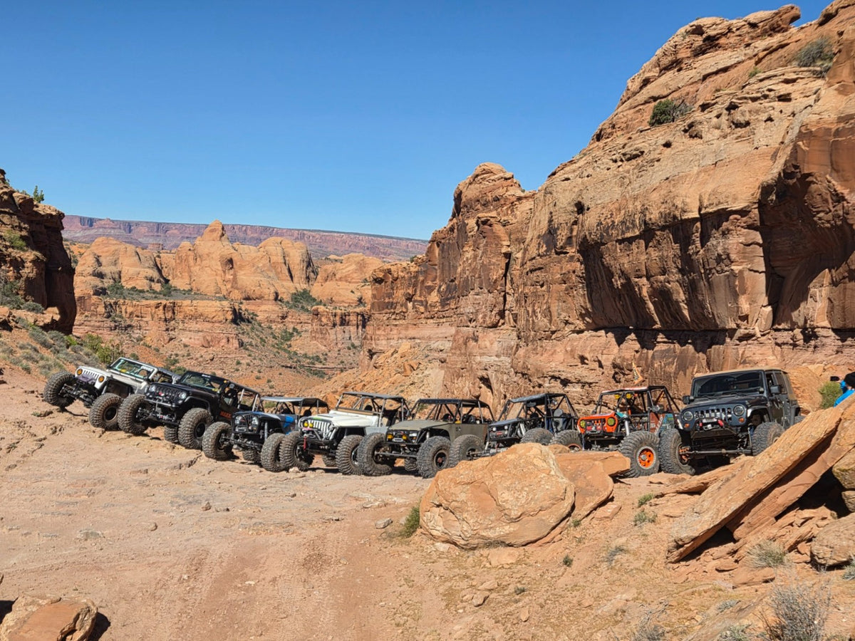 A lineup of off-road rigs on a trail in a red-rock canyon